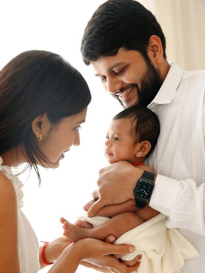 Parents smiling at their newborn, held securely in dad's hands. The focus is entirely on their connection and shared joy.