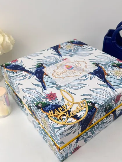 The exterior of our beautifully designed Diwali gift box, featuring a tropical parrot print and a golden "Happy Diwali" accent. This packaging is designed to impress before it's even opened.
