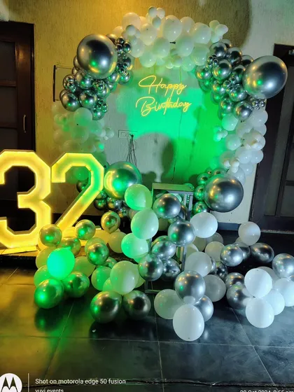 A modern birthday setup for a 32nd birthday, with a silver and white balloon arch and cool green lighting effects.