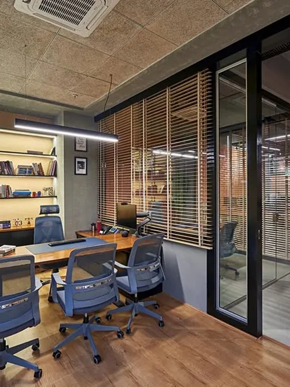 This executive cabin uses wood blinds for adjustable privacy. The design combines an industrial feel from the exposed ceiling with the warmth of wood flooring and a comfortable seating area.