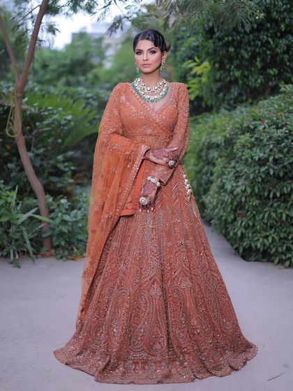 This full-length shot shows a complete party look. The elegant draping of the orange lehenga, combined with chic hair and makeup, is perfect for any wedding guest.