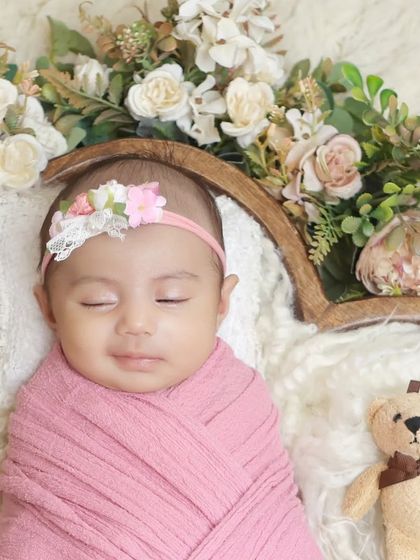 A close-up shot within a floral basket, focusing on the baby's serene expression and the delicate textures of the flowers and soft bedding.