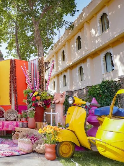 A fun photo corner with a yellow scooter and auto-rickshaw. This quirky setup, combined with the colorful backdrop, provides a perfect spot for memorable guest photos.