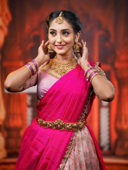 A close-up shot where the model adjusts her earrings, giving a clear view of the jhumkas and the detailed choker.