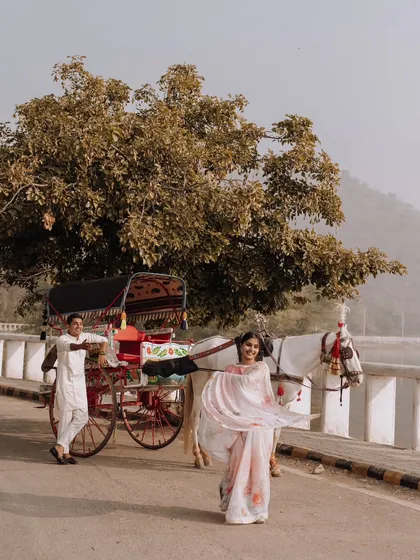 A dynamic and joyful shot of the bride twirling her saree while walking alongside a traditional horse-drawn carriage by the lake.