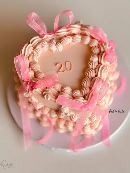 A beautiful heart-shaped cake in a soft pink hue, decorated with classic vintage Lambeth piping and delicate organza ribbons. This design is perfect for celebrating a 20th birthday in style.
