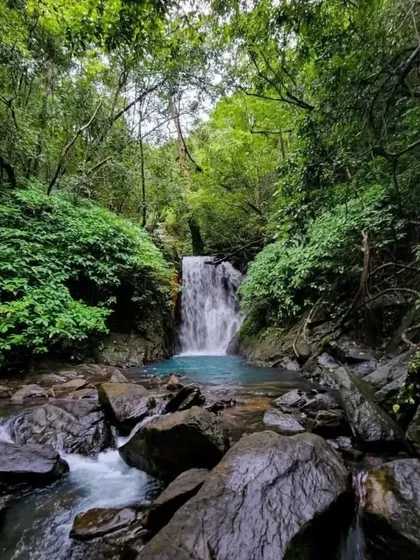 The beautiful turquoise pool at the base of an unexplored waterfall in Uttara Kannada, surrounded by lush greenery.
