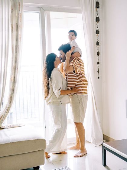 A family silhouette against a bright window, with the baby on his father's shoulders. A creative and artistic shot.