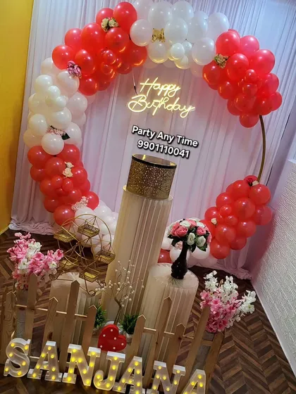 A vibrant red and white birthday theme using a circular frame for the balloon arch. The setup is personalized with light-up letters for the name "Sanjana".