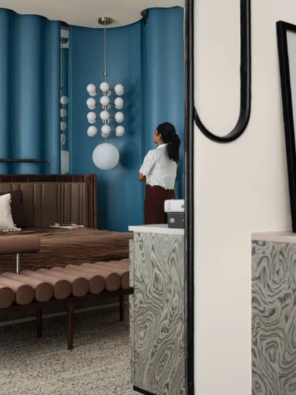 A reflection in the custom mirror shows the layers of design in the master bedroom. The blue ripple wall, the plush upholstered bench, and the statement lighting all come together to create a space that is rich in texture and personality.