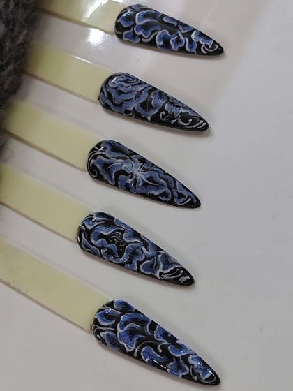 This is a practice swatch showing a sophisticated floral design. The technique involves creating layered, dimensional flowers in shades of blue over a black base, a skill we teach for creating intricate patterns.