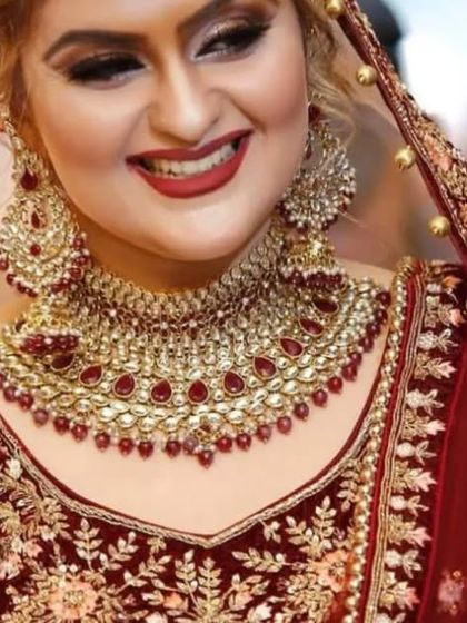 A radiant bridal portrait capturing the bride's joyful smile. The rich red of her velvet lehenga and the sparkle of her jewelry are vibrant and full of life.