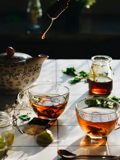 A beautiful, sunlit shot of tea being served. The backlighting makes the tea and the honey drip glow, creating an abstract and artistic image that is also warm and inviting.