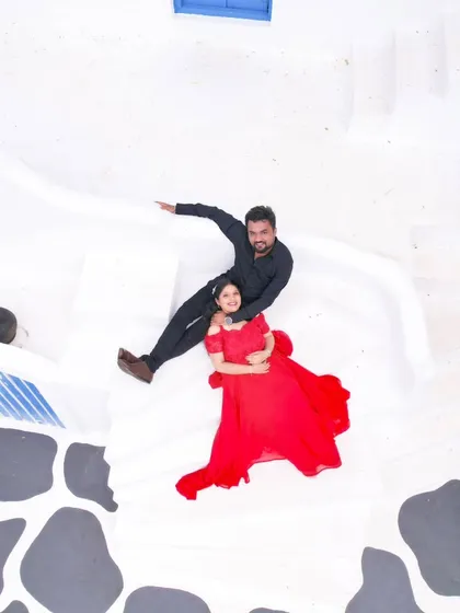 An aerial view of the couple at our Santorini set. The bride's red dress stands out against the white architecture, making for a stunning pre-wedding photo.