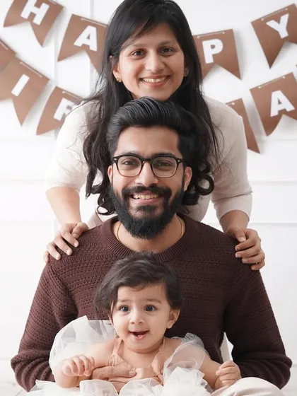 A playful 'human totem pole' family portrait, with the baby, father, and mother stacked up and smiling for a fun birthday photo.