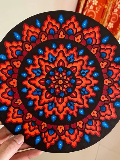 This piece uses a fiery palette of red, orange, and blue on a black background. The contrasting colors create a dynamic and eye-catching circular mandala design.