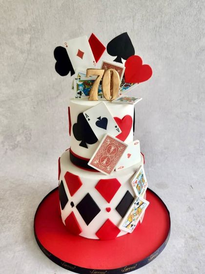 A dramatic casino-themed cake for a 70th birthday bash. The design features a cascade of edible playing cards and a bold red, black, and white colour scheme.