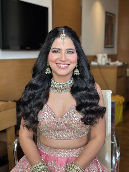 A happy engagement bride with her hair styled in beautiful, healthy-looking waves and a center part with a maang tikka.