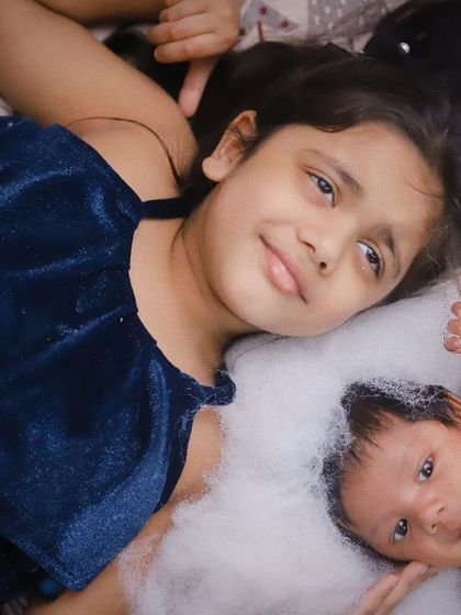 A beautiful portrait of sibling love. The older sister looks on protectively as her newborn sibling rests beside her.