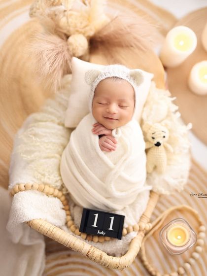 A top-down view of a sleeping newborn in a white swaddle and bear-ear bonnet, creating a heartwarming and angelic portrait.