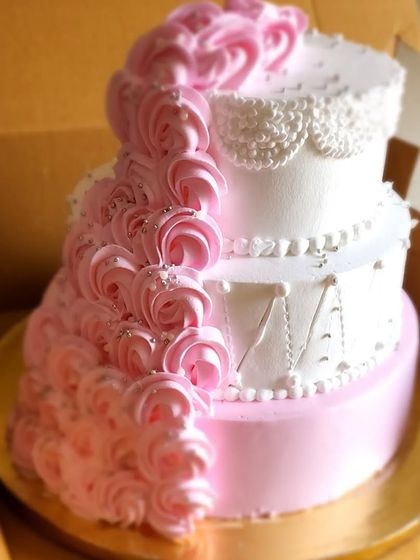 An elegant three-tier engagement cake ready to join the party. The design features a cascade of pink buttercream rosettes and delicate lace-like piping, combining classic and modern styles.