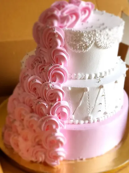 An elegant three-tier engagement cake ready to join the party. The design features a cascade of pink buttercream rosettes and delicate lace-like piping, combining classic and modern styles.
