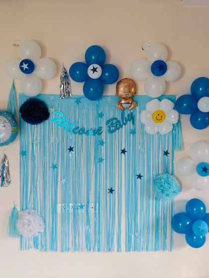 A close-up of a 'Welcome Baby' wall decoration, featuring a blue shimmer curtain and star-accented balloon flowers.