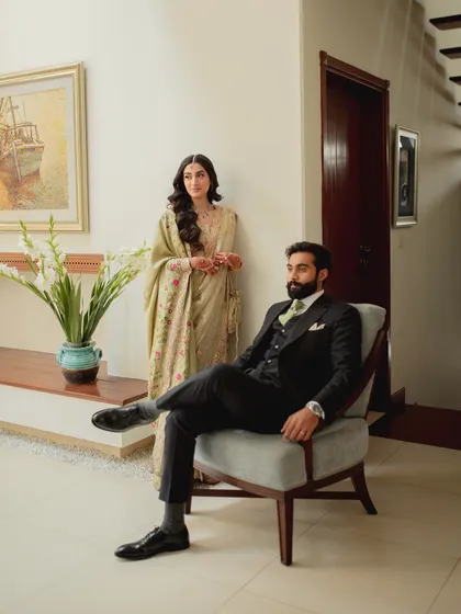 Modern love with a touch of classic style. This portrait captures the couple in a chic indoor setting, with the groom seated and the bride standing behind him, creating a look that is both fashionable and intimate.