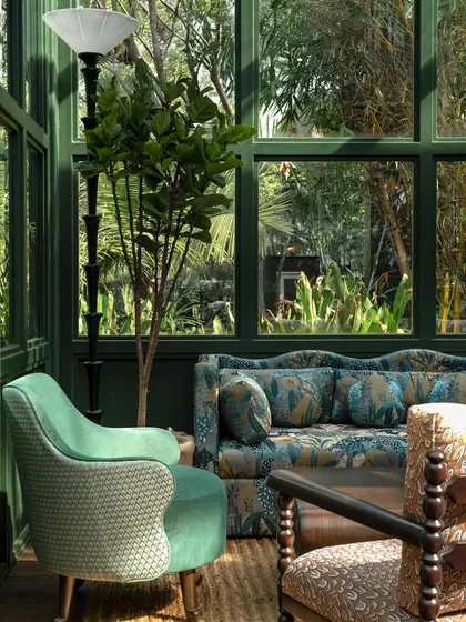 A detail of the furniture, where modern and classic forms are mixed. A floral-printed sofa is paired with a contemporary armchair, all unified by a palette of greens.