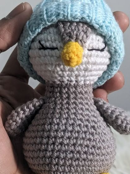 A tiny, sleepy penguin wearing a blue hat, held in my hand to show its small size.