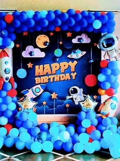 A detailed outer space theme for a 7th birthday. The backdrop is a starry sky with planets, framed by blue balloons, with rocket and astronaut props to create an immersive galaxy experience.