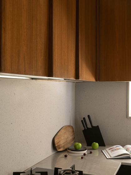 A close-up of the kitchen, highlighting the sleek, handleless design of the wooden upper cabinets and the subtle texture of the backsplash.