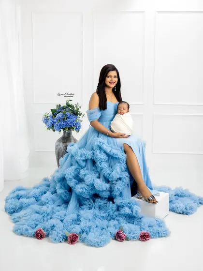 A stunning full-length portrait of a mother in a flowing blue gown, holding her newborn. This showcases a more glamorous style for post-maternity photos.