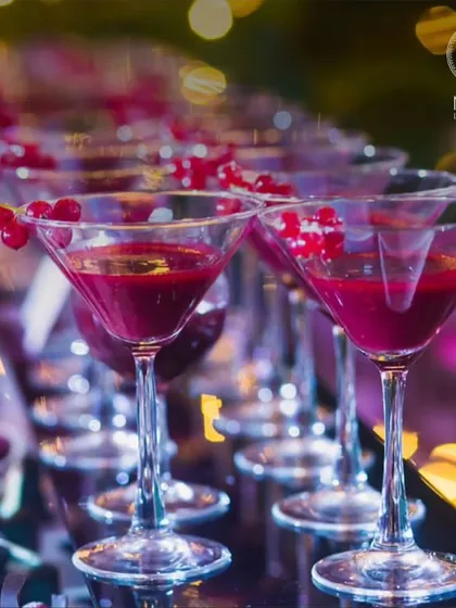 A row of beautiful crimson cocktails in martini glasses, garnished with red currants. A refreshing drink is the perfect way to start a party, and we craft ours to be as beautiful as they are delicious.