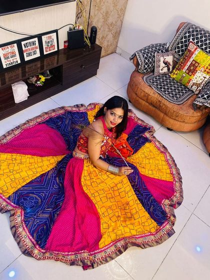 A model posing with her patchwork Garba lehenga spread out, holding a small orange pouch.
