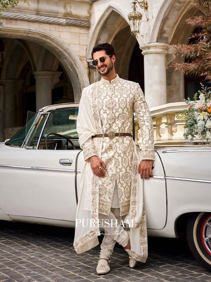 A symphony of tradition and modern grace. This groom, laughing by a vintage car, wears an intricately embroidered sherwani that tells a story of grandeur and love.