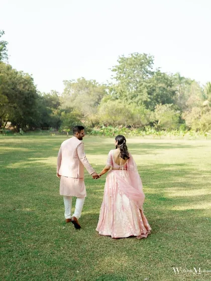 The couple walks hand-in-hand through a green lawn, a simple yet beautiful portrait of their journey together. The soft colors and natural setting add to the romantic feel.