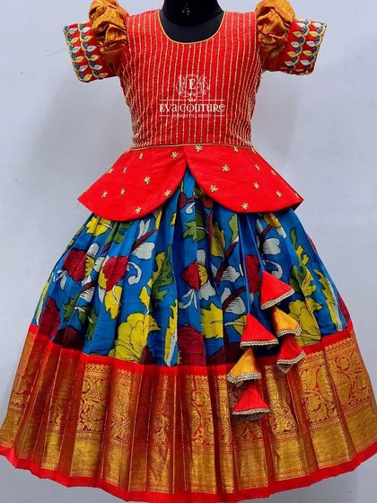 A vibrant Kalamkari lehenga. The red blouse has striped detailing, and the skirt has a colorful blue, red, and yellow print.