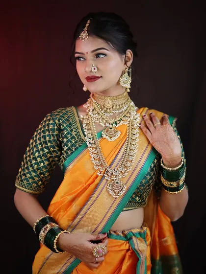 A classic portrait of a Maharashtrian bride. The combination of the orange and green saree with heavy jewelry is timeless, and the makeup is designed to balance it all perfectly.
