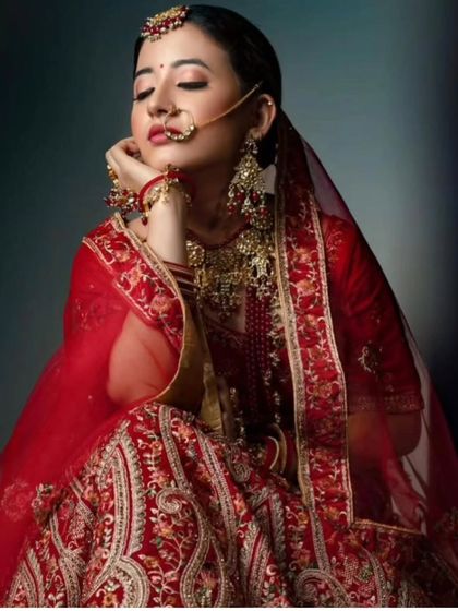 An artistic shot of a bride in a red lehenga, wearing a traditional red-beaded jewellery set. The pose highlights the delicate nath and jhumkas.