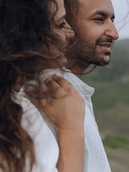 A close-up candid shot with the wind blowing through the bride's hair as she leans on her partner, creating a natural and romantic feel.