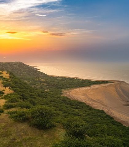 An aerial view of the coastline at Dholavira in Gujarat. The image captures the unique meeting of the salt marsh and the sea at sunset.