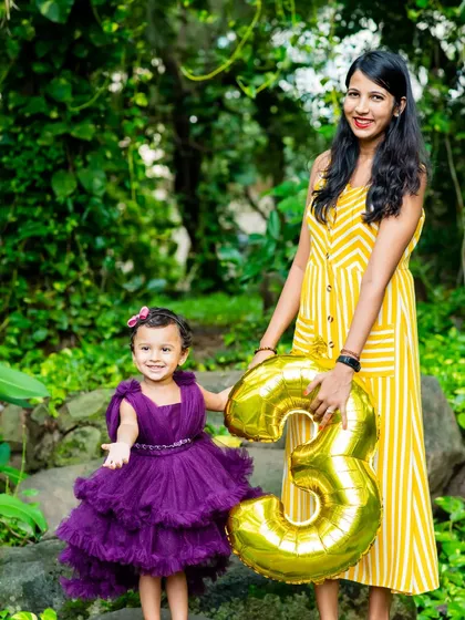 A mother and daughter pose together with a '3' balloon in a lush, green park setting.
