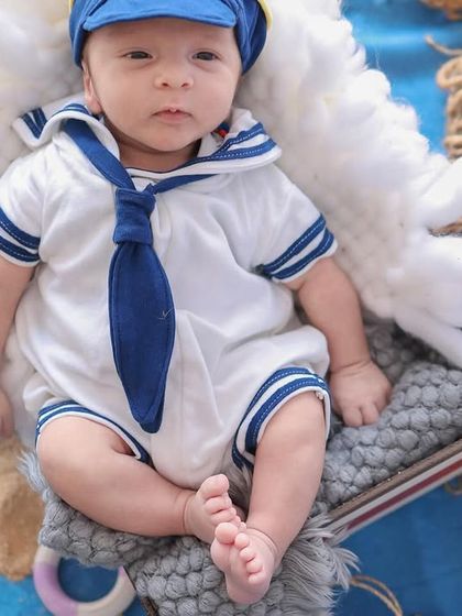 A close-up portrait of the baby in his adorable sailor costume, showing the details of his outfit and his calm, observant expression.