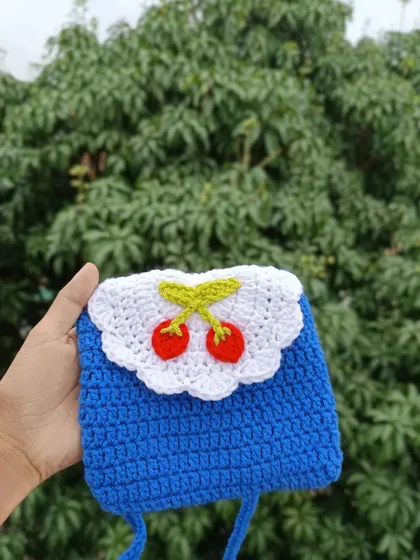 A vibrant blue phone sling bag with a cherry applique on a white scalloped flap. This is a fun, colorful design perfect for a youthful brand.