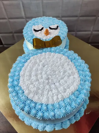 A cute character cake shaped like an owl or penguin, made with blue and white piped buttercream.