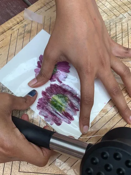 The moment of creation. Hands carefully hold the flower in place while hammering, ensuring a clear and beautiful print is transferred onto the greeting card.