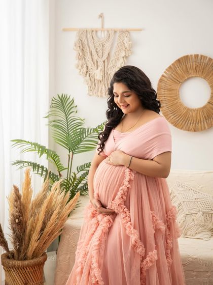 A tender moment, looking down at her baby bump. The soft pink tones and natural light create a peaceful and loving atmosphere.