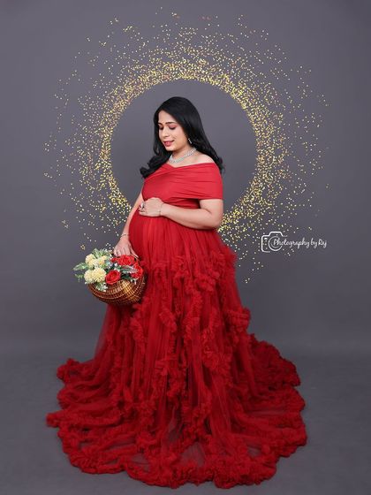 A lovely studio portrait of a mother-to-be in a red ruffled gown, holding a basket of flowers.