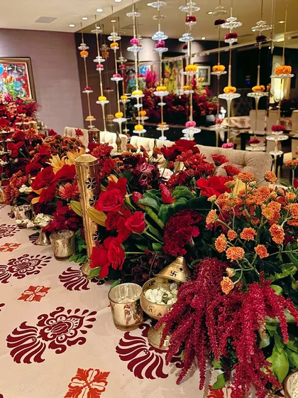 A luxurious Diwali tablescape, featuring a runner of red and orange flowers, traditional brass lamps, and hanging floral strings.